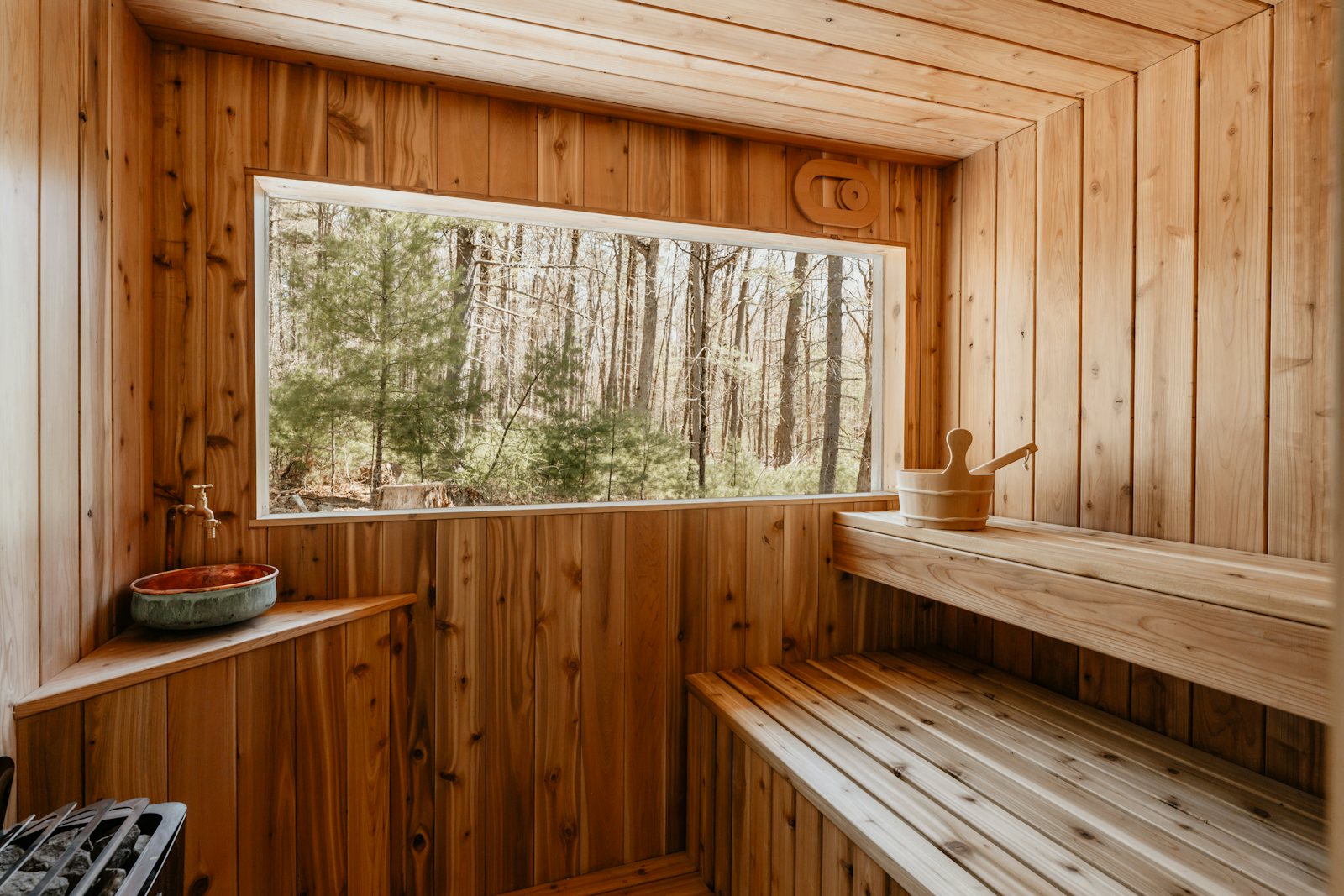 A calm wooden sauna interior with a bench and a large window overlooking a forest.